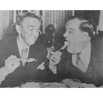 Comedian Stan Laurel feeds a sliced banana to his partner, Oliver Hardy, at the Netherland Plaza hotel during their visit in 1942, Hilton Cincinnati Netherland Plaza in Cincinnati, Ohio.