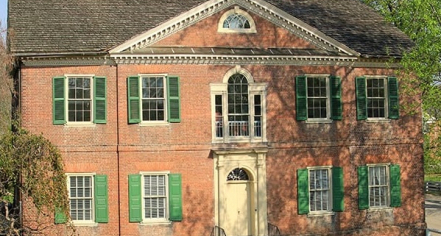 Image Of A Two Story Brick Building With White Trimmed Windows And Green Shutters, As Well As A Yellow Front Door.