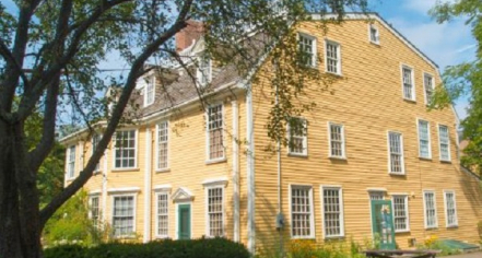 Image Of A Four-story Yellow House With White Trimmed Windows Surrounded By Trees.